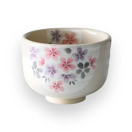 The Kohiki Pink Sakura Ceramic Matcha Bowl is a white ceramic bowl adorned with floral patterns in pink, purple, and gray on a black background, ideal for a traditional matcha tea ceremony.