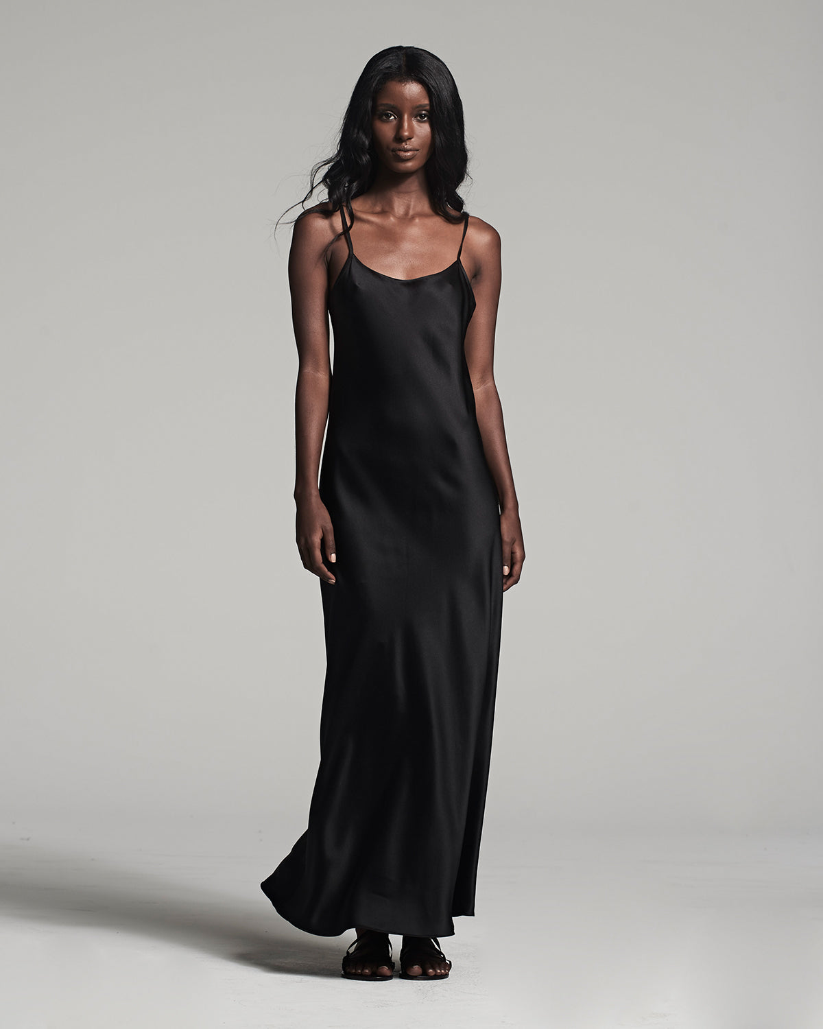 Woman wearing a black slip dress against a gray background
