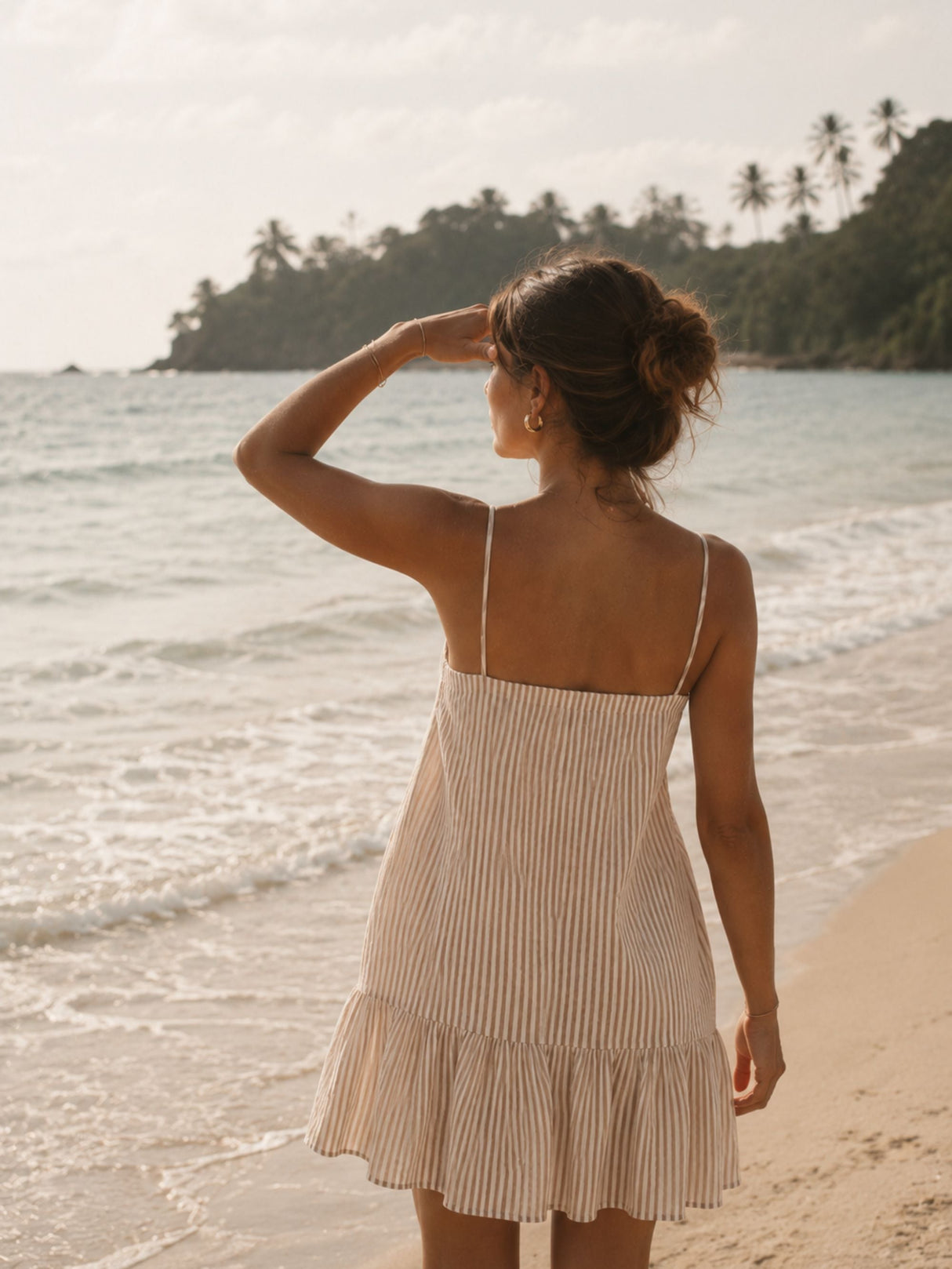 Woman in a striped dress standing on a beach with palm trees in the background