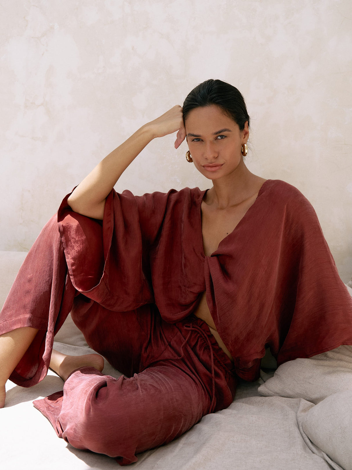 Woman wearing a red outfit sitting on a bed with a neutral background