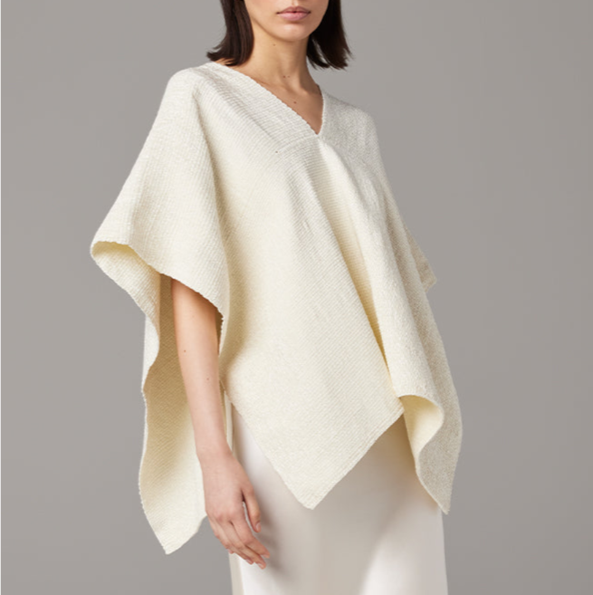 Woman wearing a cream-colored poncho against a gray background