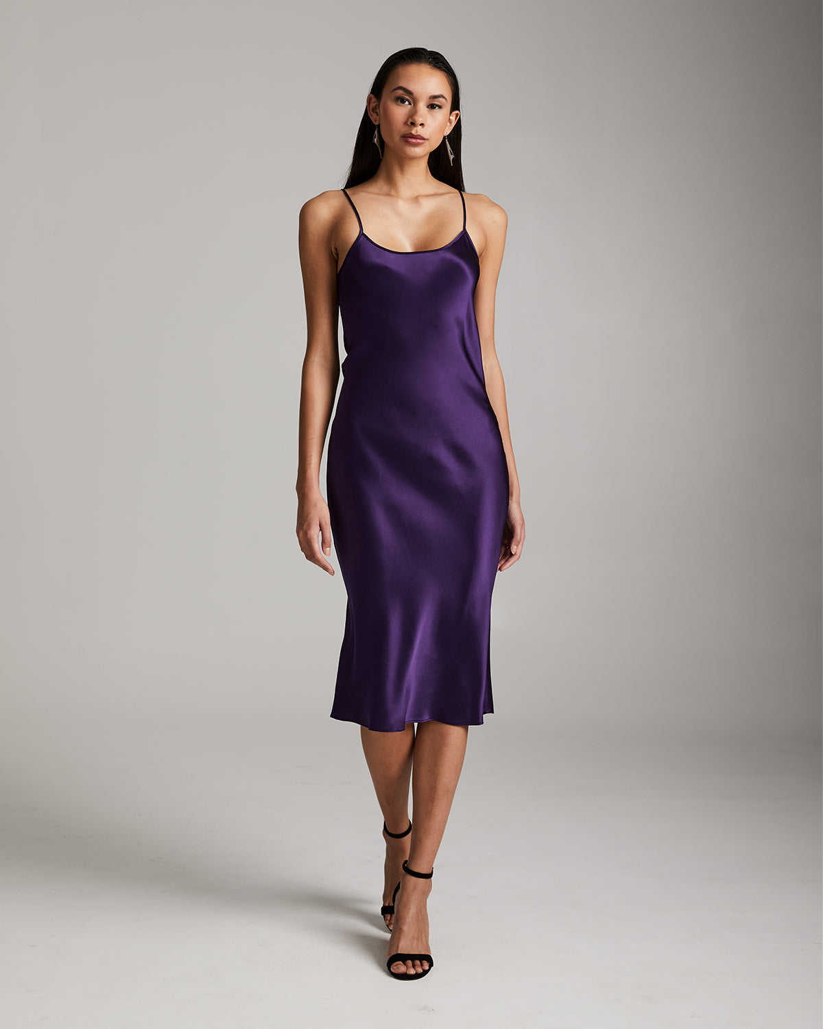 Woman wearing a purple satin slip dress against a gray background