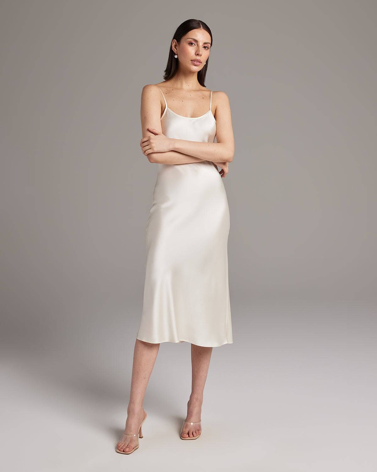 Woman wearing a white satin slip dress against a plain background