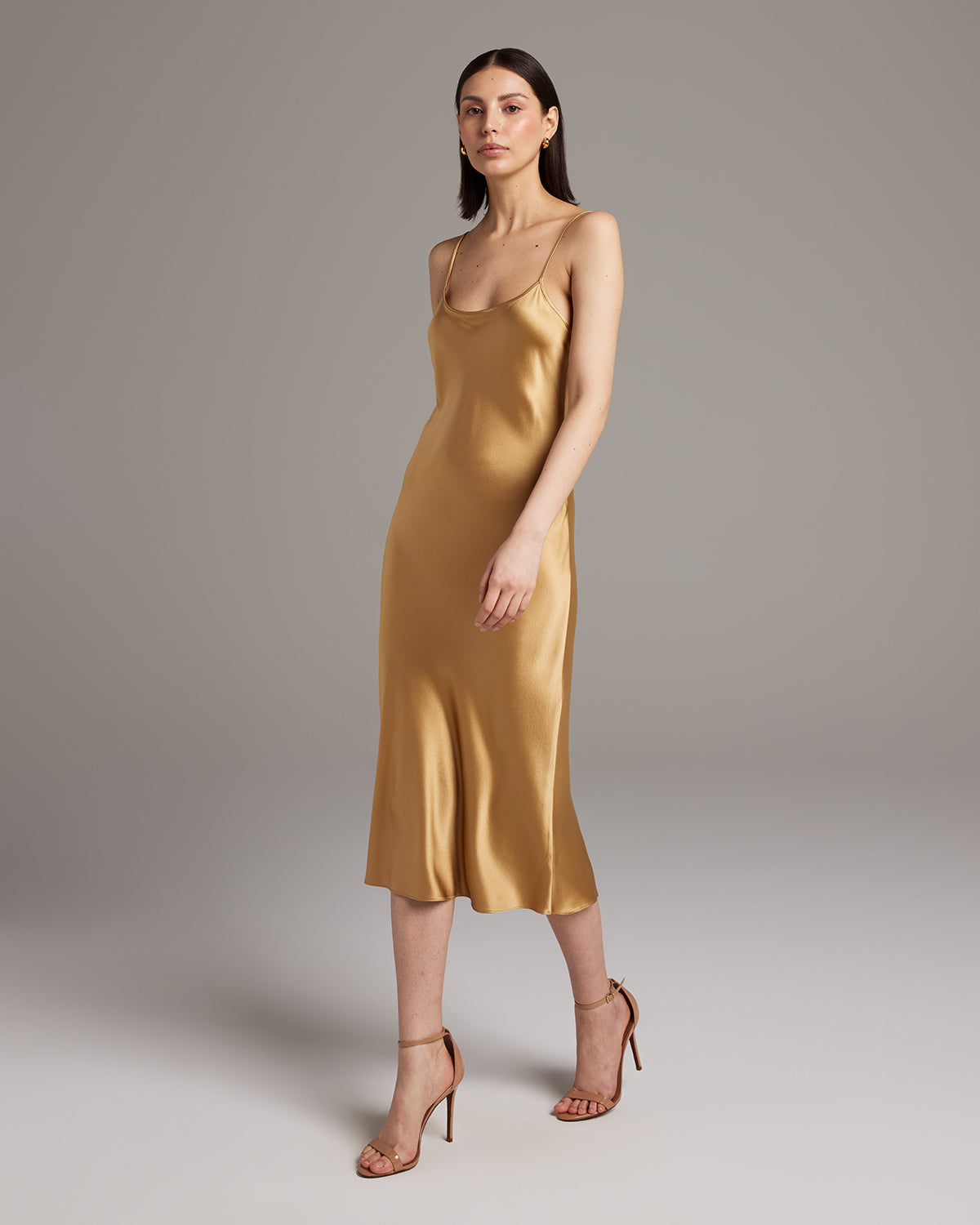 Woman wearing a gold satin slip dress against a plain background