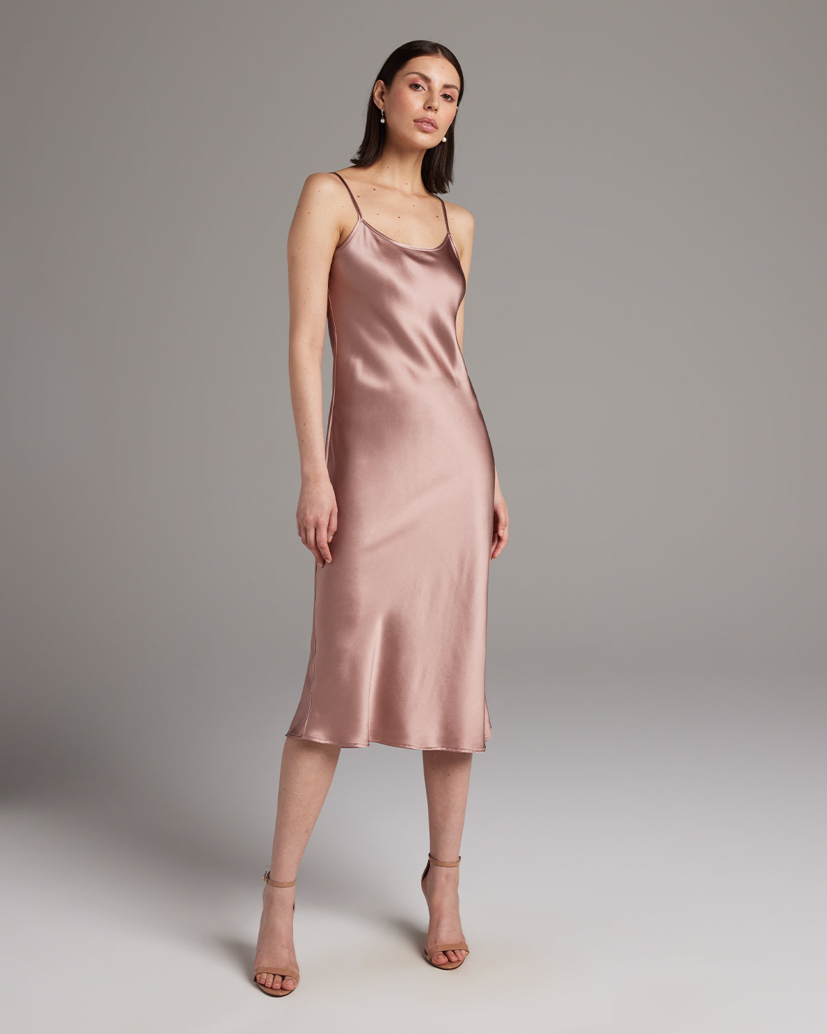 Woman wearing a pink satin slip dress against a plain background