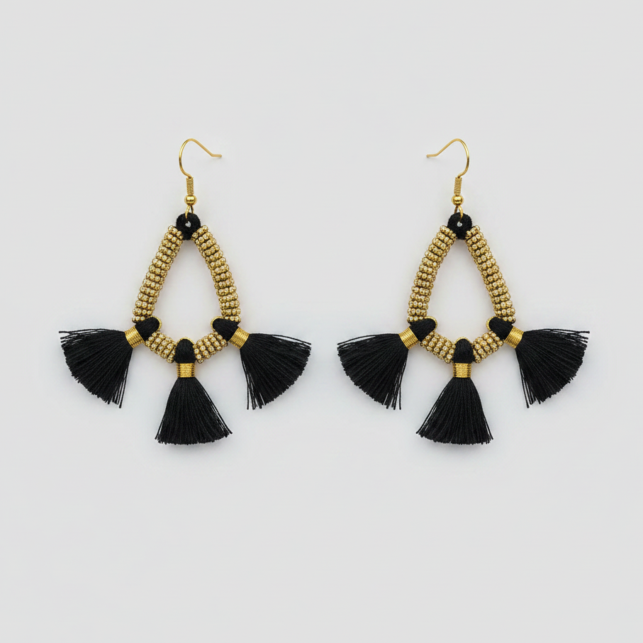 Pair of gold beaded earrings with black tassels on a light gray background