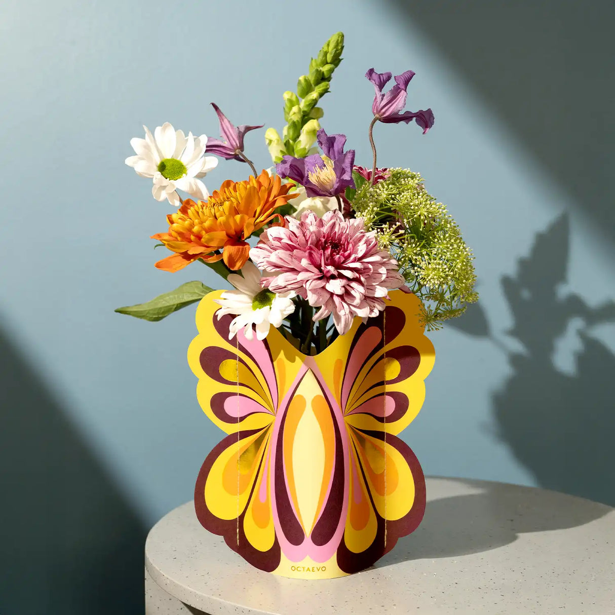 Colorful bouquet in a decorative butterfly-shaped vase against a blue wall.