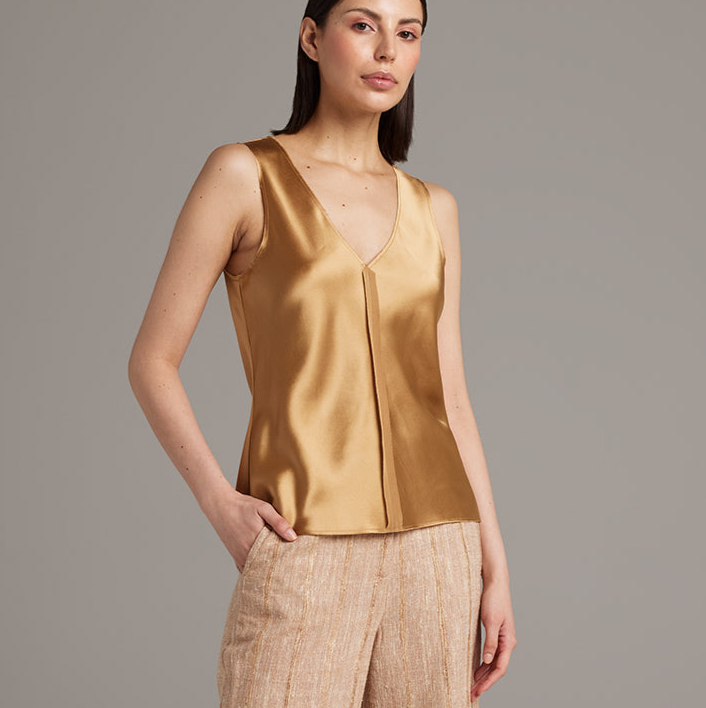 Woman wearing a gold sleeveless top against a gray background