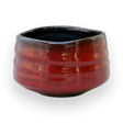 The Red Matcha Bowl features a red glaze and a rounded, slightly uneven shape, evoking the essence of traditional Minoyaki Pottery, set against a black background.