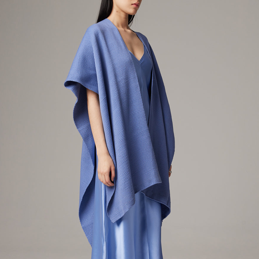 Woman wearing a blue poncho against a gray background