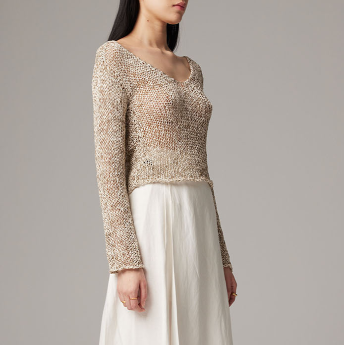 Woman wearing a textured beige sweater over a white dress on a gray background