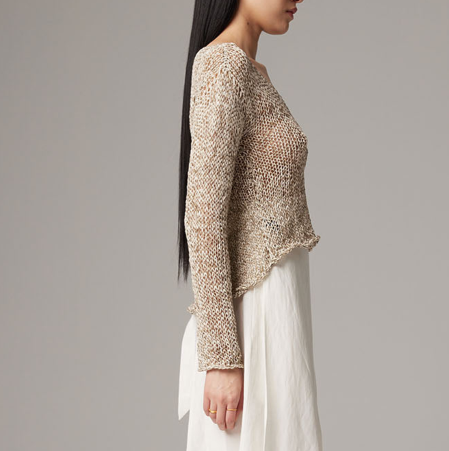 Woman wearing a textured beige sweater and white pants against a gray background