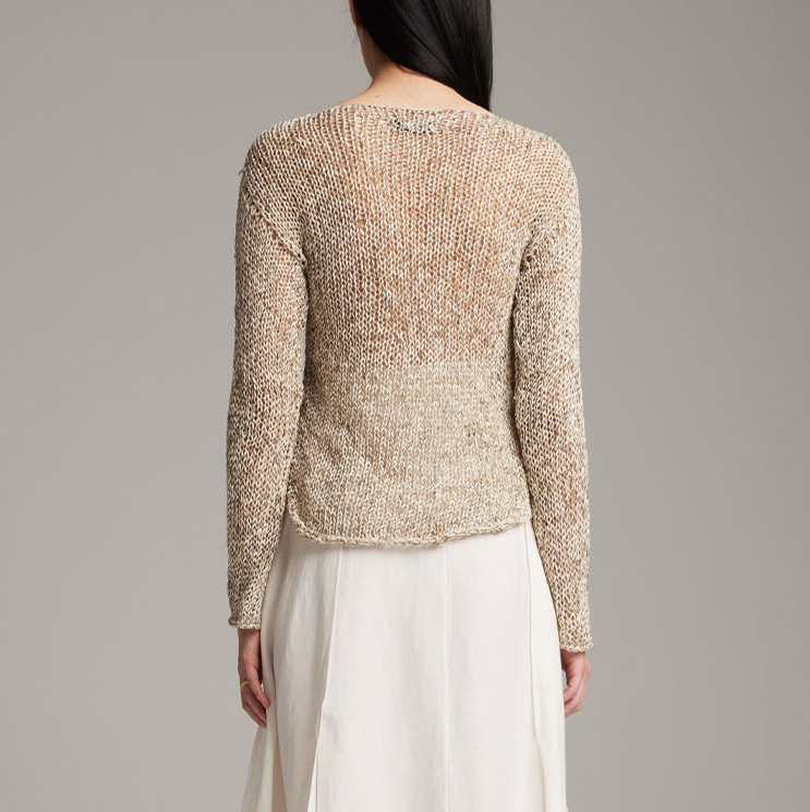 Person wearing a textured beige sweater and white pants against a gray background