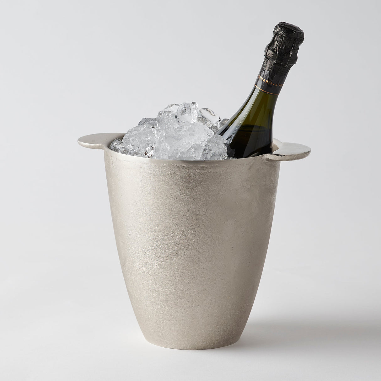 A silver aluminum wine chiller bucket with a 750 ml bottle of wine inside, surrounded by ice.