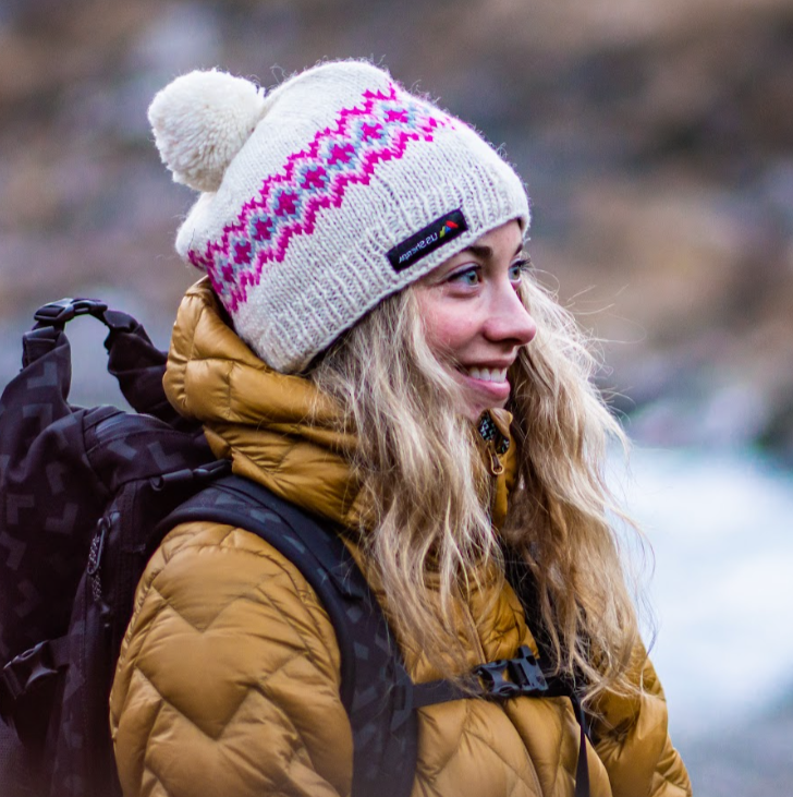 Person wearing a patterned knit hat and yellow jacket with a blurred natural background