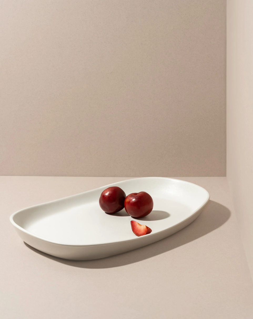 White oval platter with three red plums on a beige background