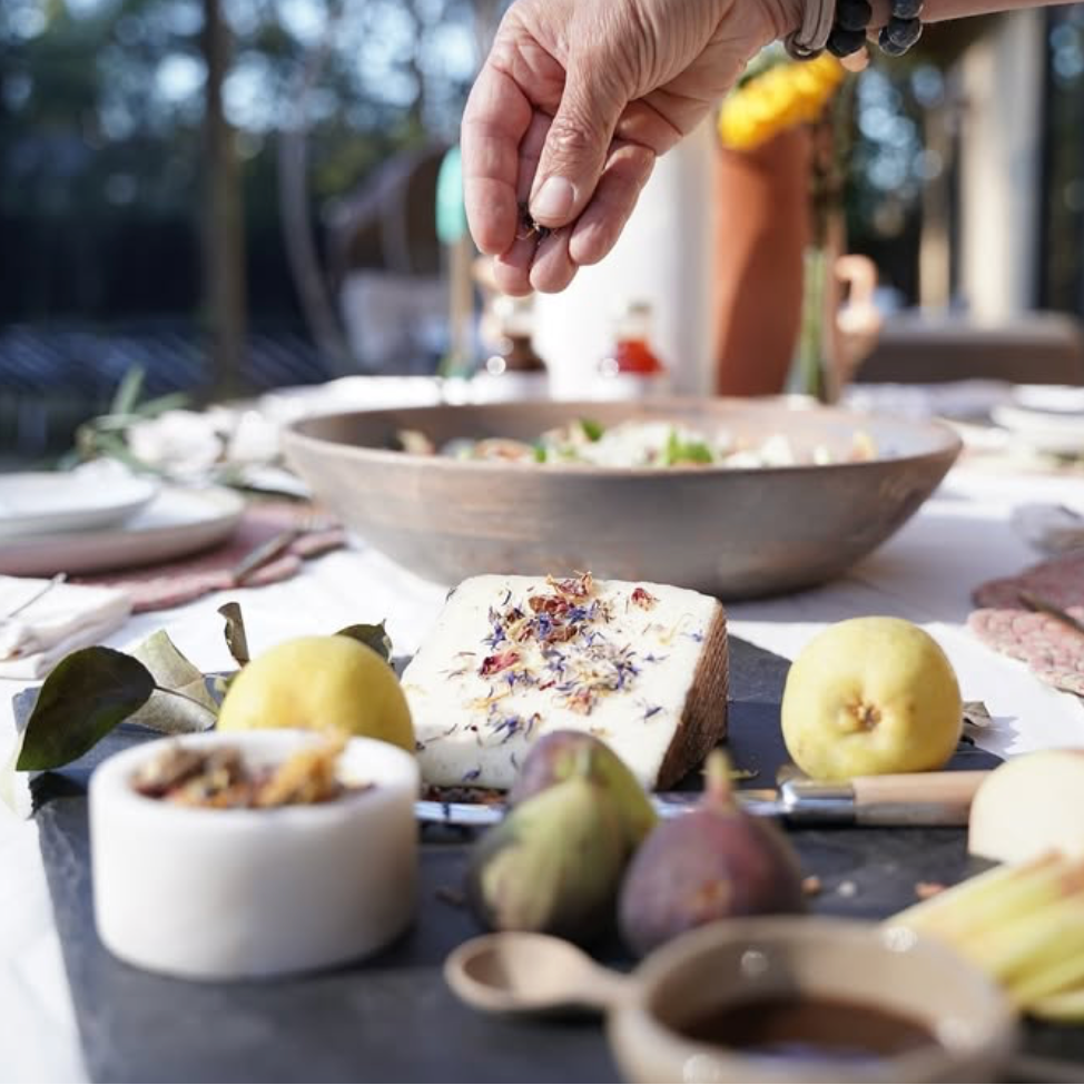 Person preparing a dish at an outdoor table with various food items and a blurred background