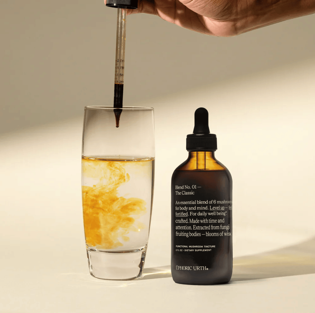 Bottle of tincture with dropper being used to add liquid to a glass on a neutral background