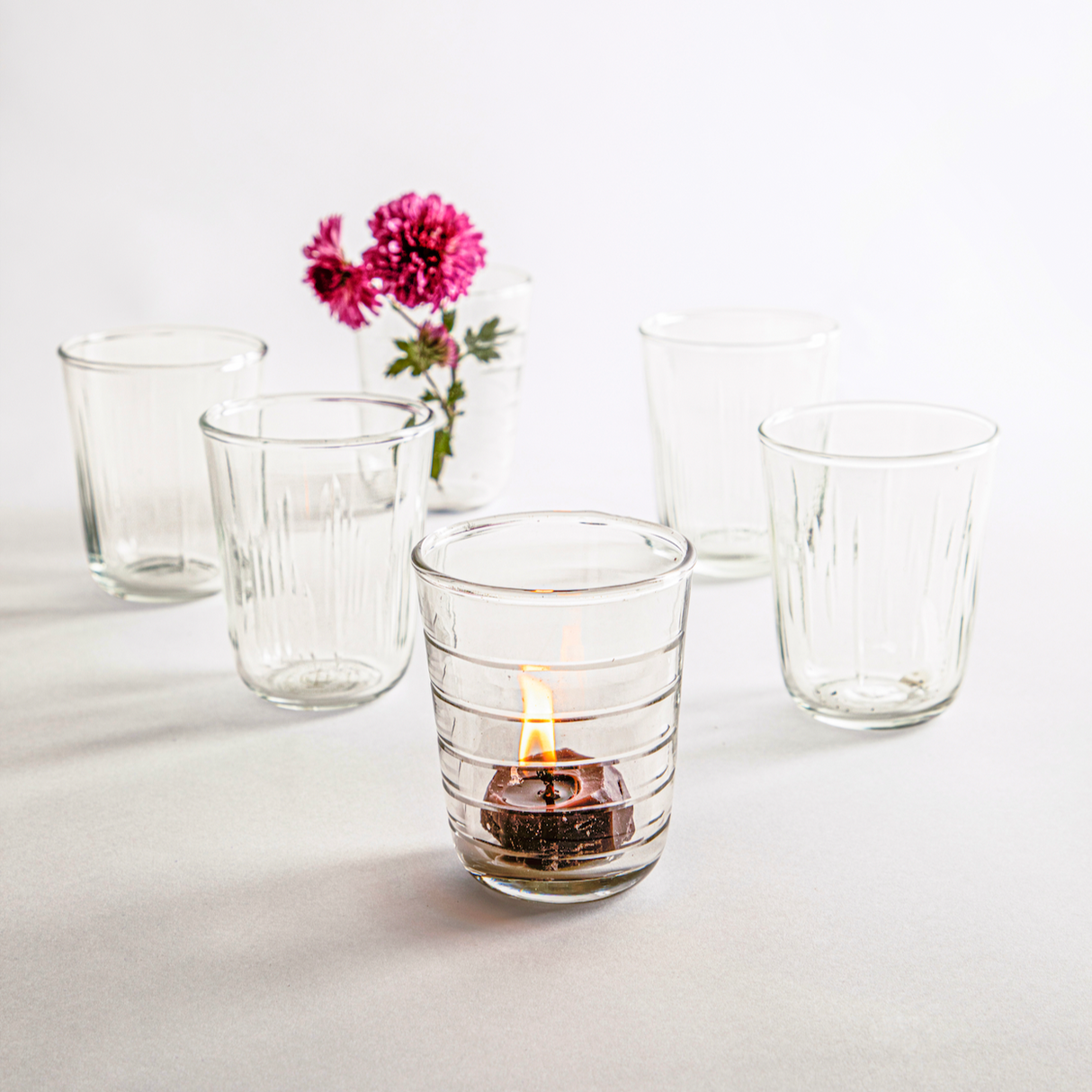 A set of clear glass etched short glasses with various hand-carved groove patterns, displayed alongside a pink flower.
