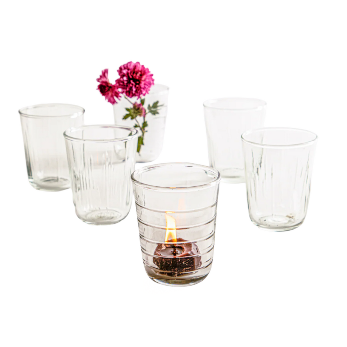 Set of clear glass tumblers with a lit candle and pink flowers on a white background