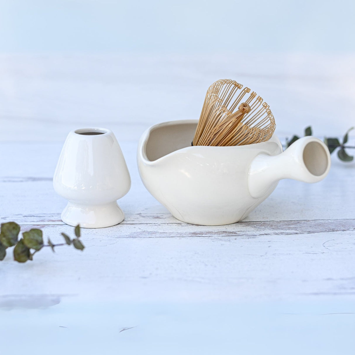 White Ceramic Matcha Bowl with Spout set on a white wooden surface, beautifully accented with eucalyptus sprigs. An ideal housewarming gift inspired by the Japanese tea ceremony.