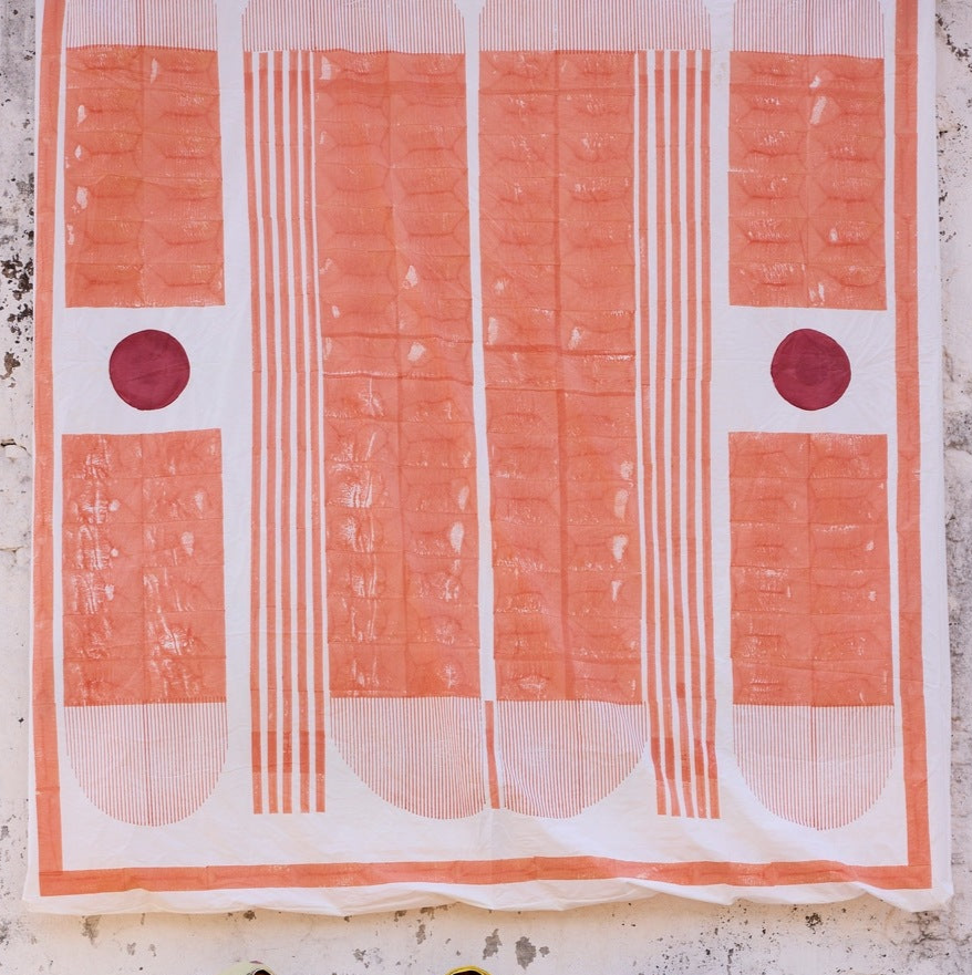 Three women in colorful traditional attire standing in front of a large fabric display with geometric patterns.