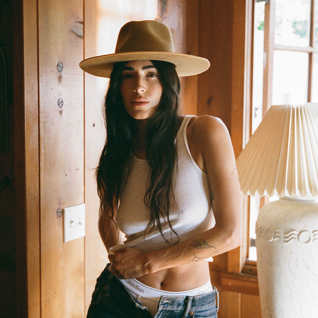 Woman wearing a beige hat indoors with wooden walls and a lamp in the background