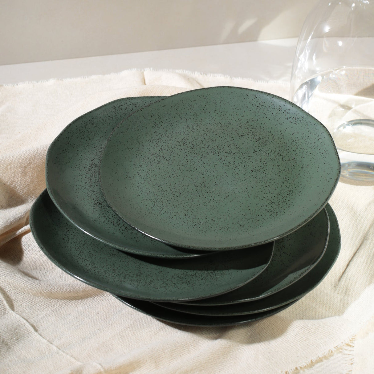 Set of three green ceramic plates stacked on a light fabric surface