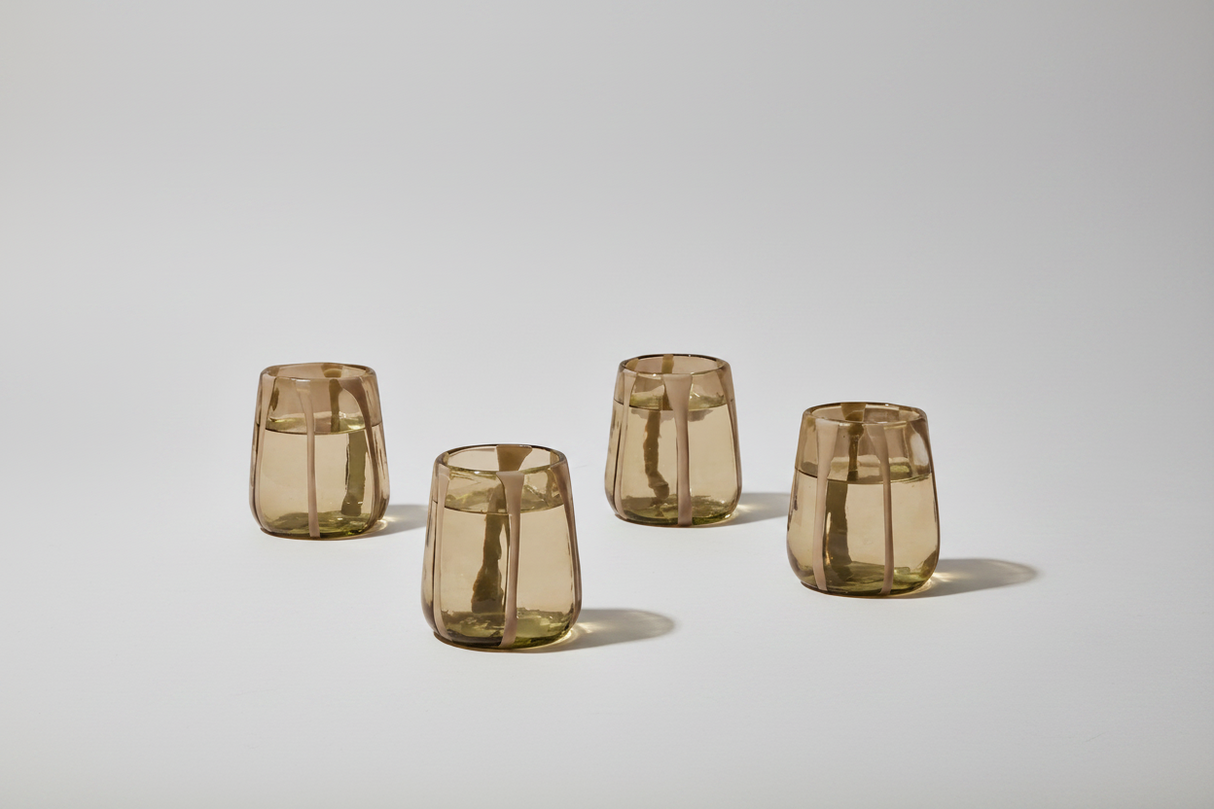 Four transparent brown glass tumblers on a light gray background