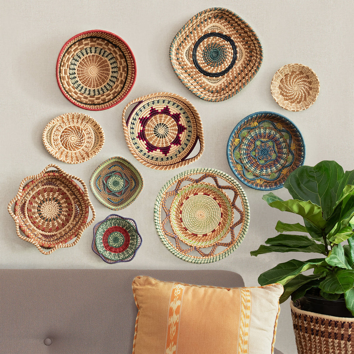 Decorative woven baskets of various sizes and colors on a wall with a plant and cushion in the foreground.