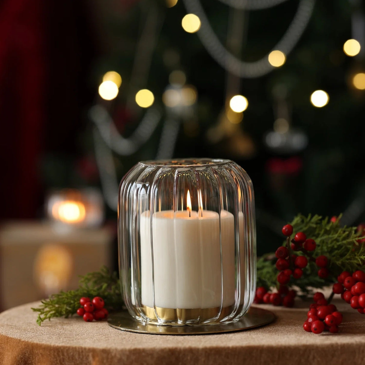 Candle in a glass holder on a table with a Christmas tree in the background