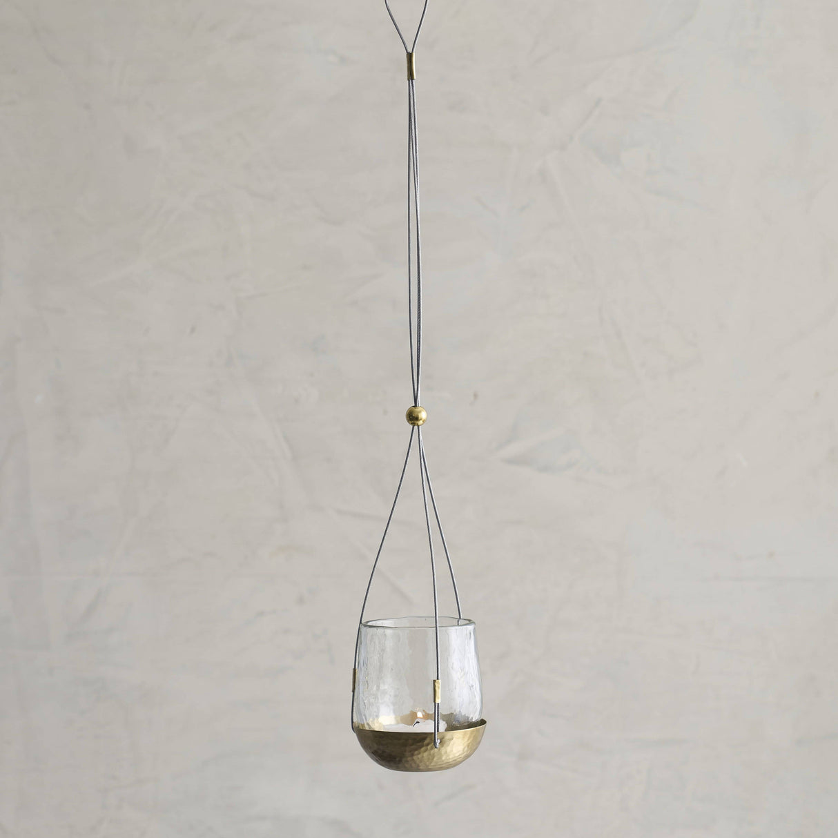 Hanging glass lantern with brass base on a plain background