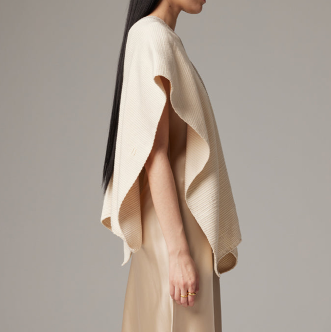 Woman wearing a beige knitted poncho against a plain background