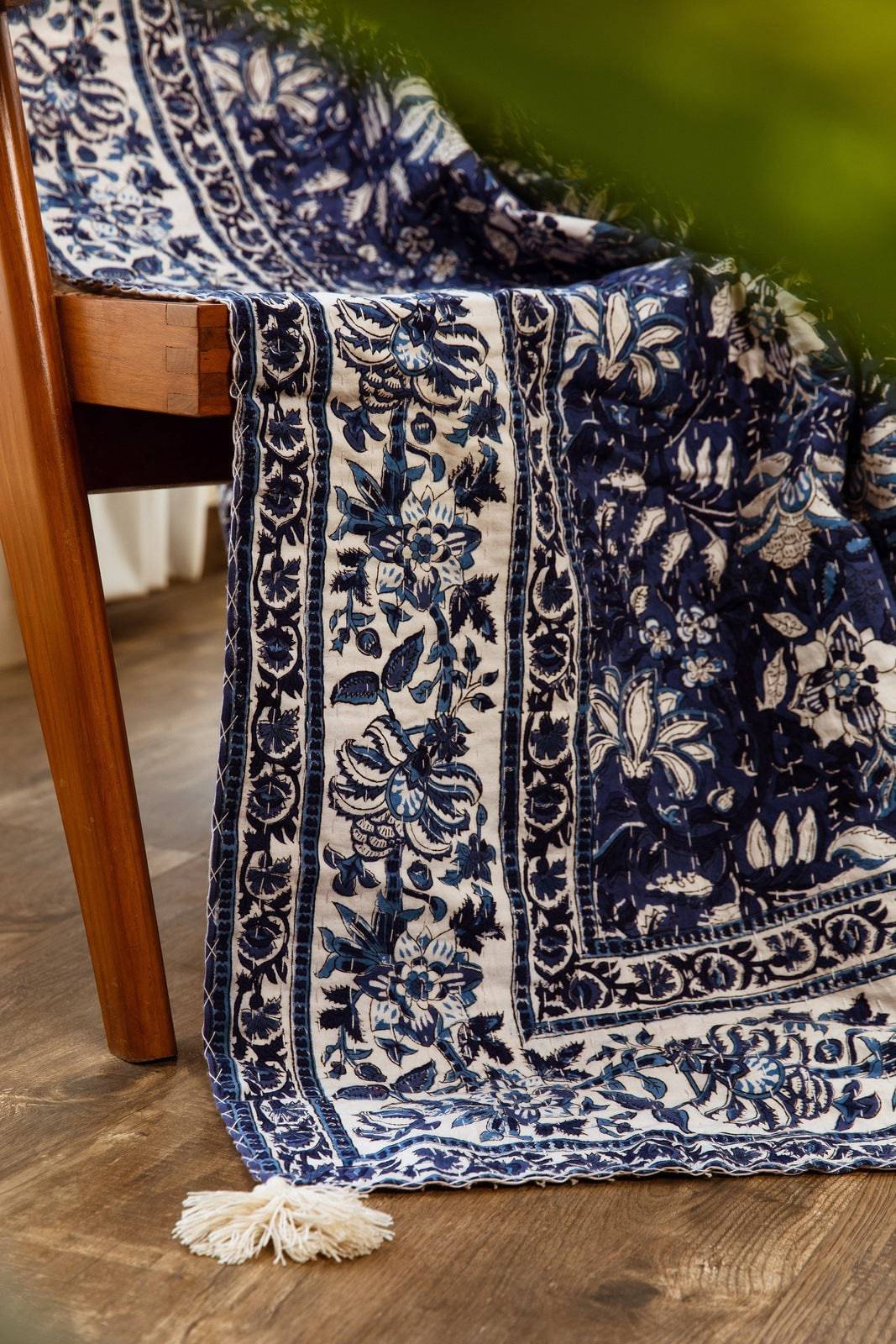Blue and white patterned blanket draped over a wooden chair on a wooden floor.