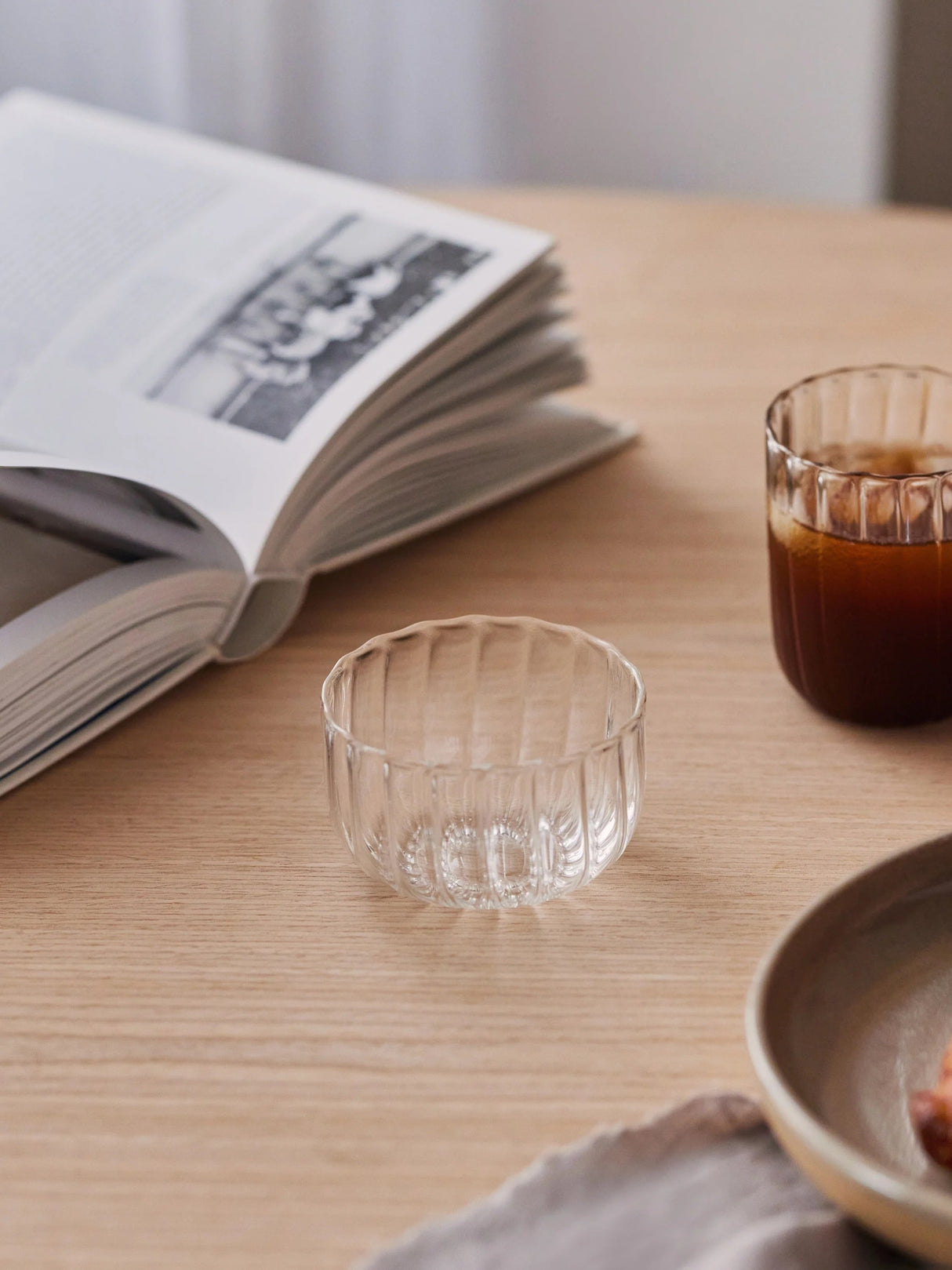 Clear glass cup on a wooden table with an open book and a small bowl in the background.