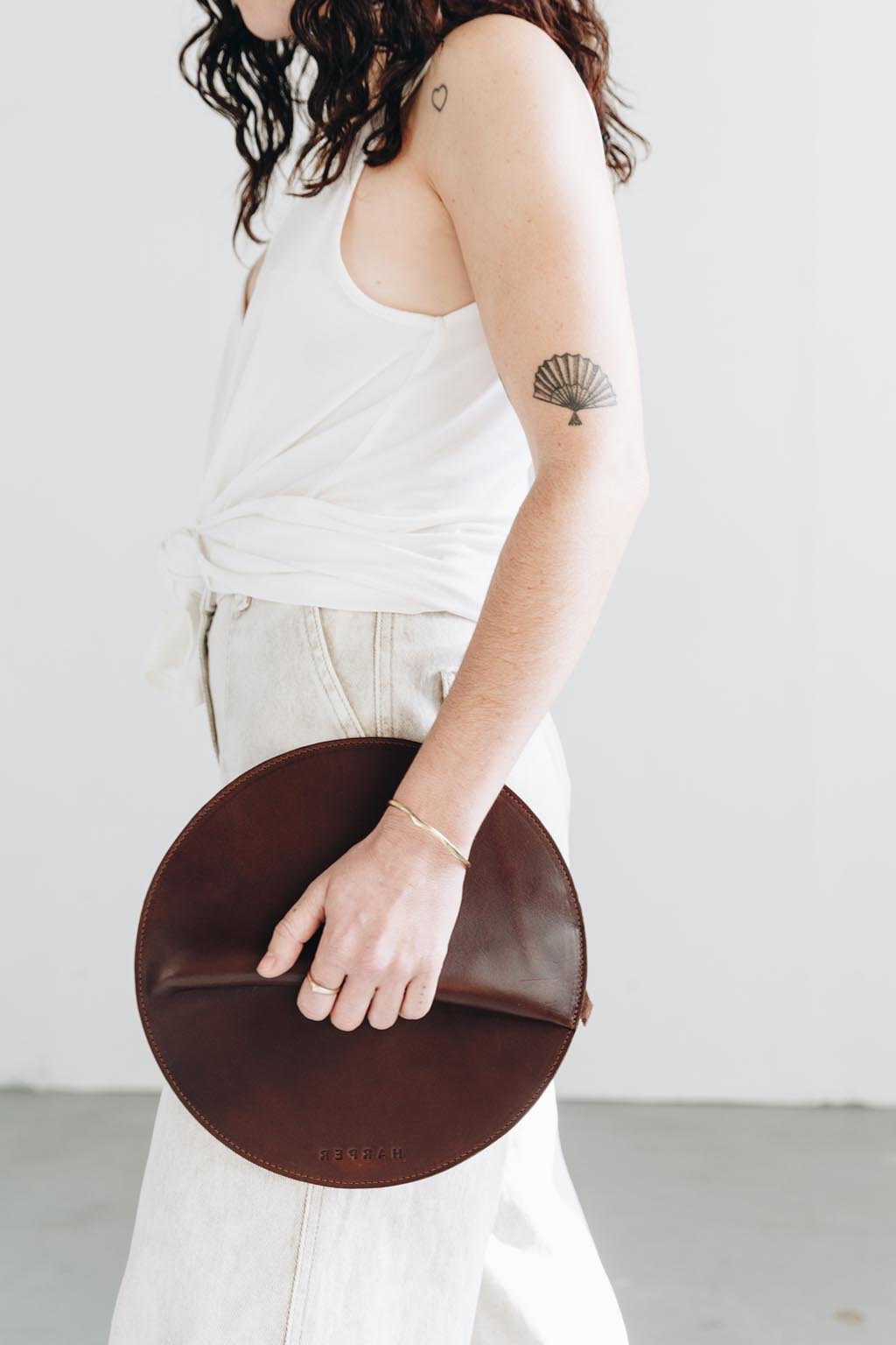 Person holding a brown circular clutch against a white background