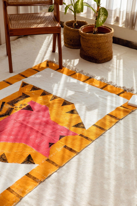 Quilt with geometric pattern on a white floor with plants and a chair in the background