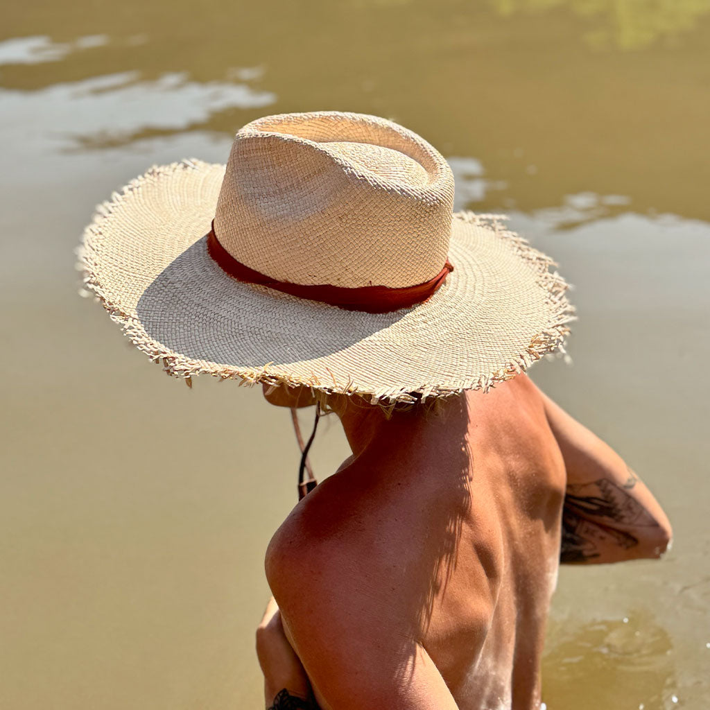 Person wearing a straw hat with a red band by a body of water