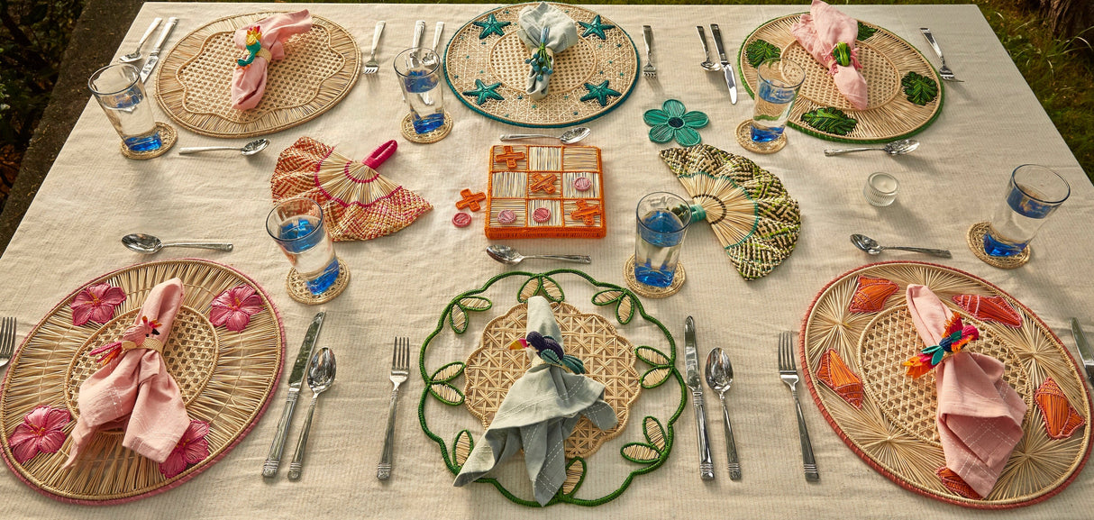Dining table set with wicker placemats, cutlery, and decorative items outdoors.