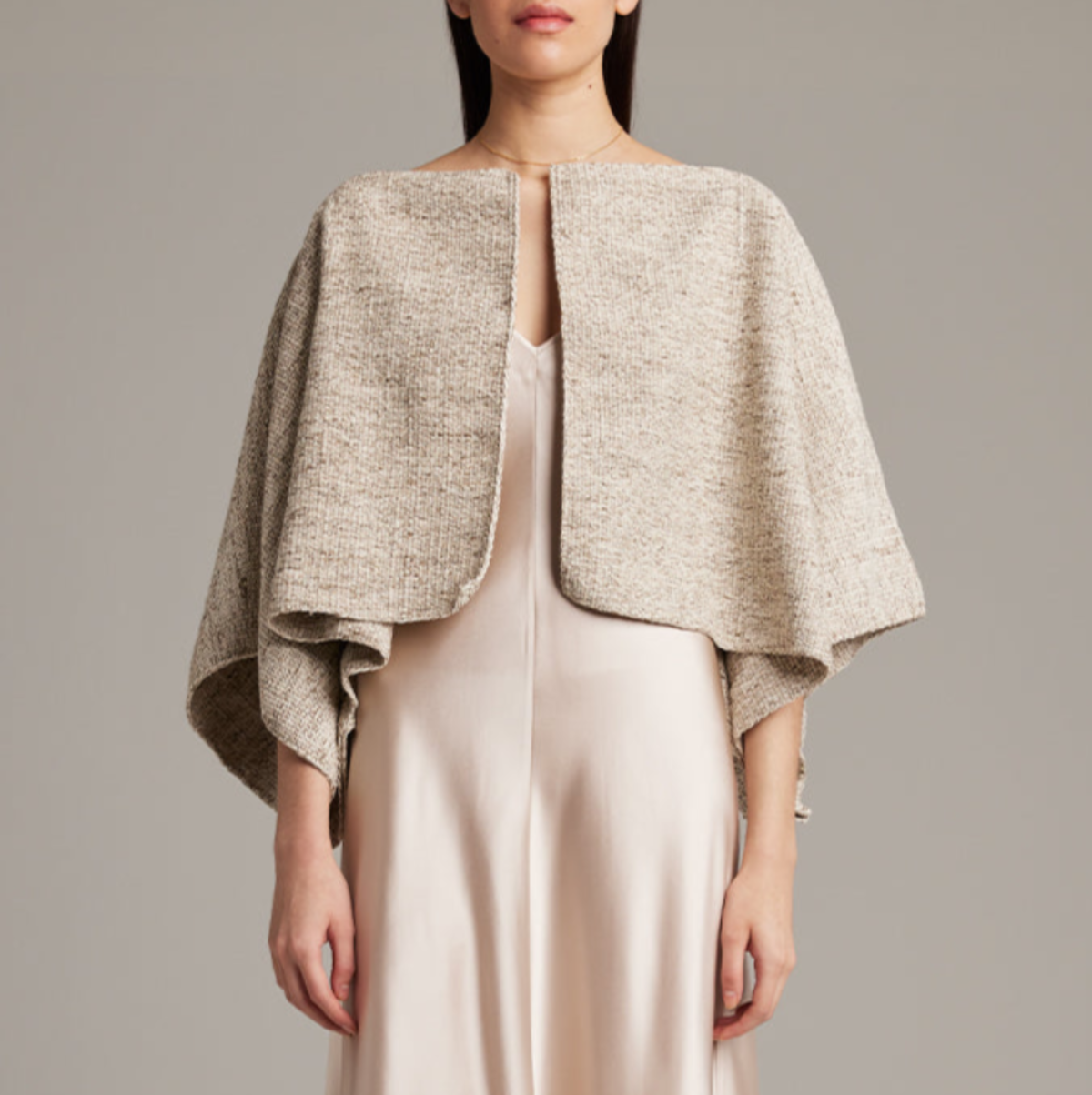Woman wearing a beige textured shrug over a plain dress against a neutral background