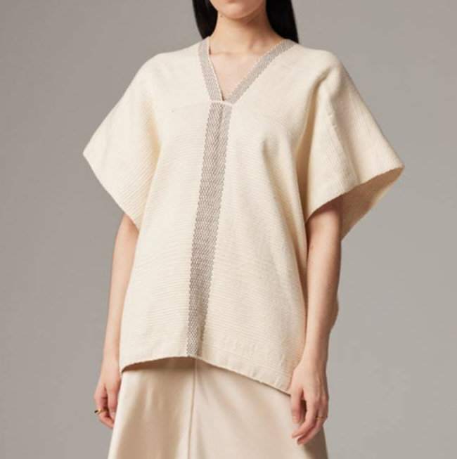 Woman wearing a beige knit poncho against a gray background