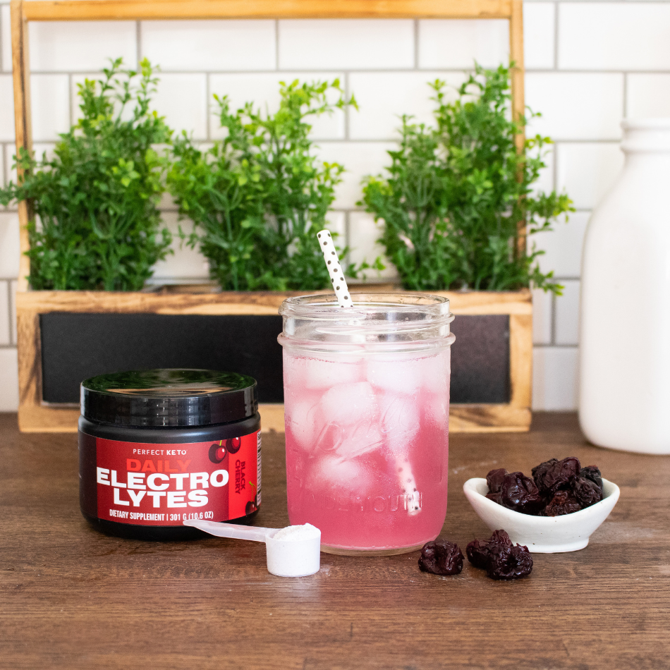 Pink iced drink in a mason jar with a straw, next to a jar labeled 'Electrolytes' on a wooden surface with plants in the background.