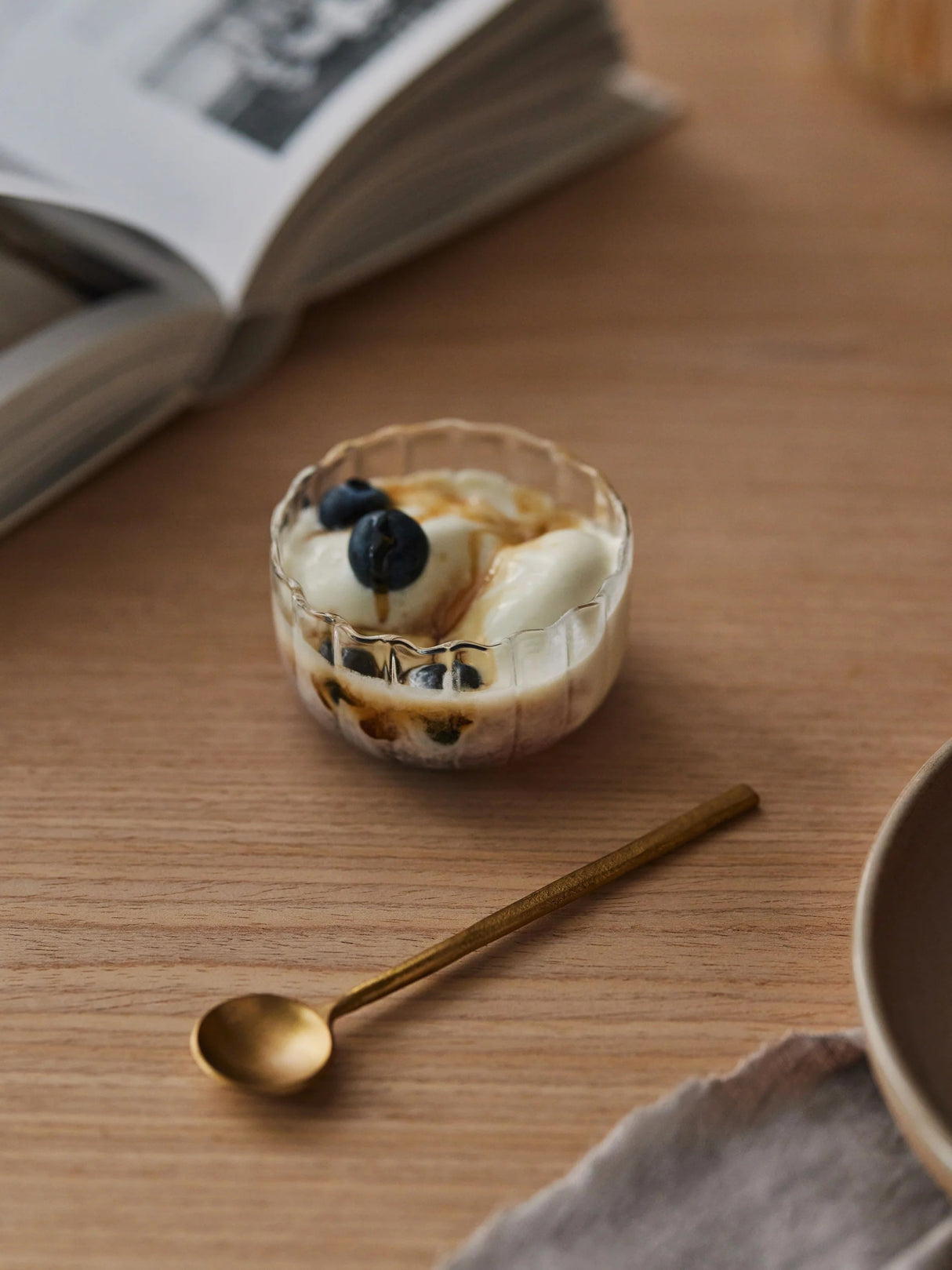 Small dessert with whipped cream and blueberries in a glass bowl on a wooden table with a gold spoon.