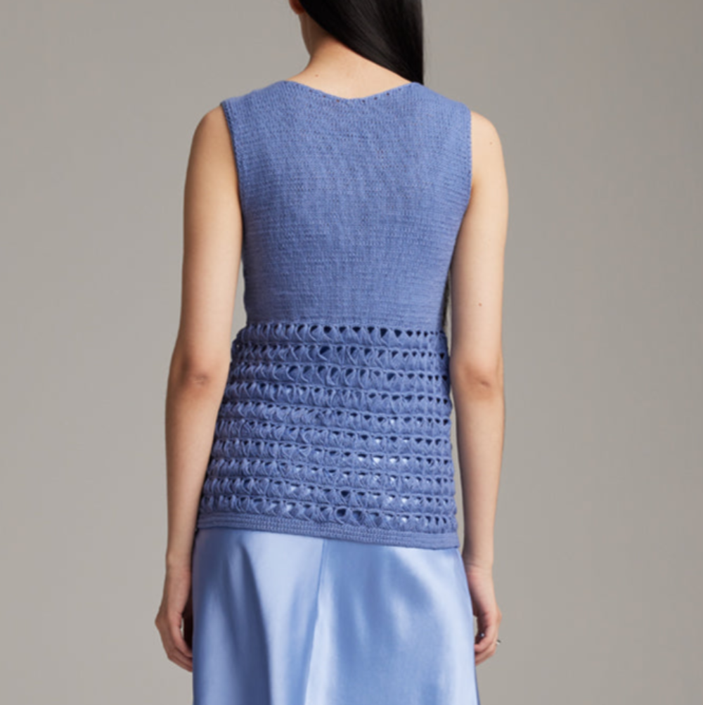 Person wearing a blue sleeveless top with a textured pattern on a plain background