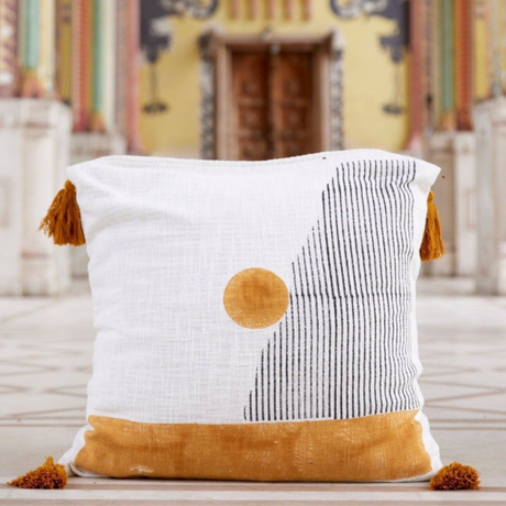 Decorative pillow with white, black, and orange design on a wooden surface.