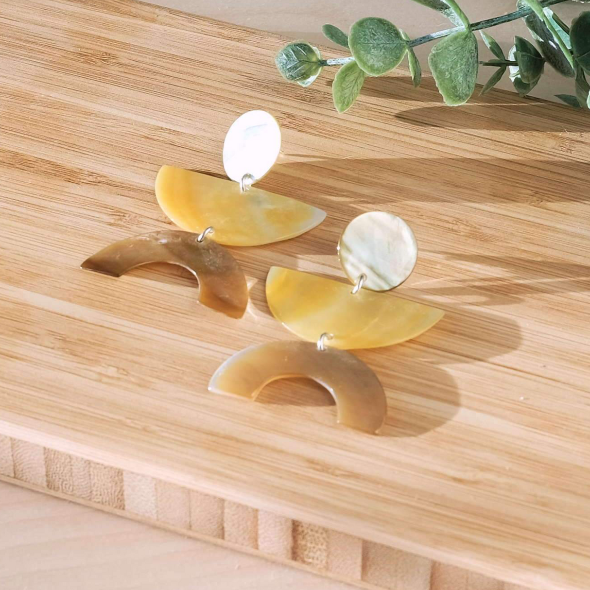 Set of earrings on a wooden surface with a plant in the background