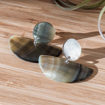 Pair of earrings on a wooden surface with a plant in the background