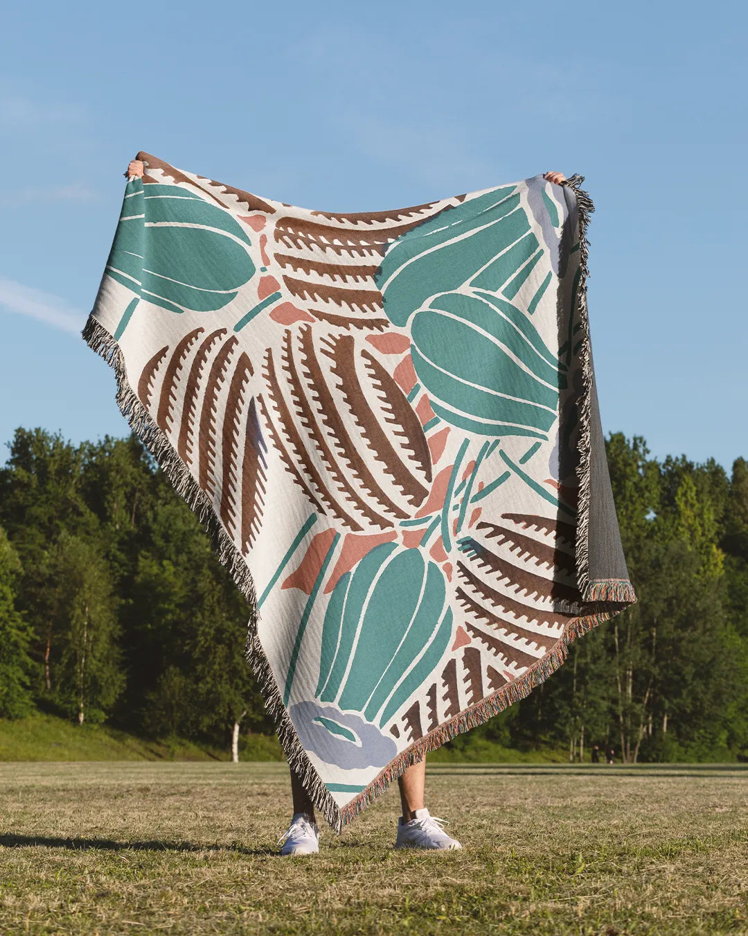 Desert-inspired woven throw blanket with cactus and floral patterns in earthy green, brown, and beige.