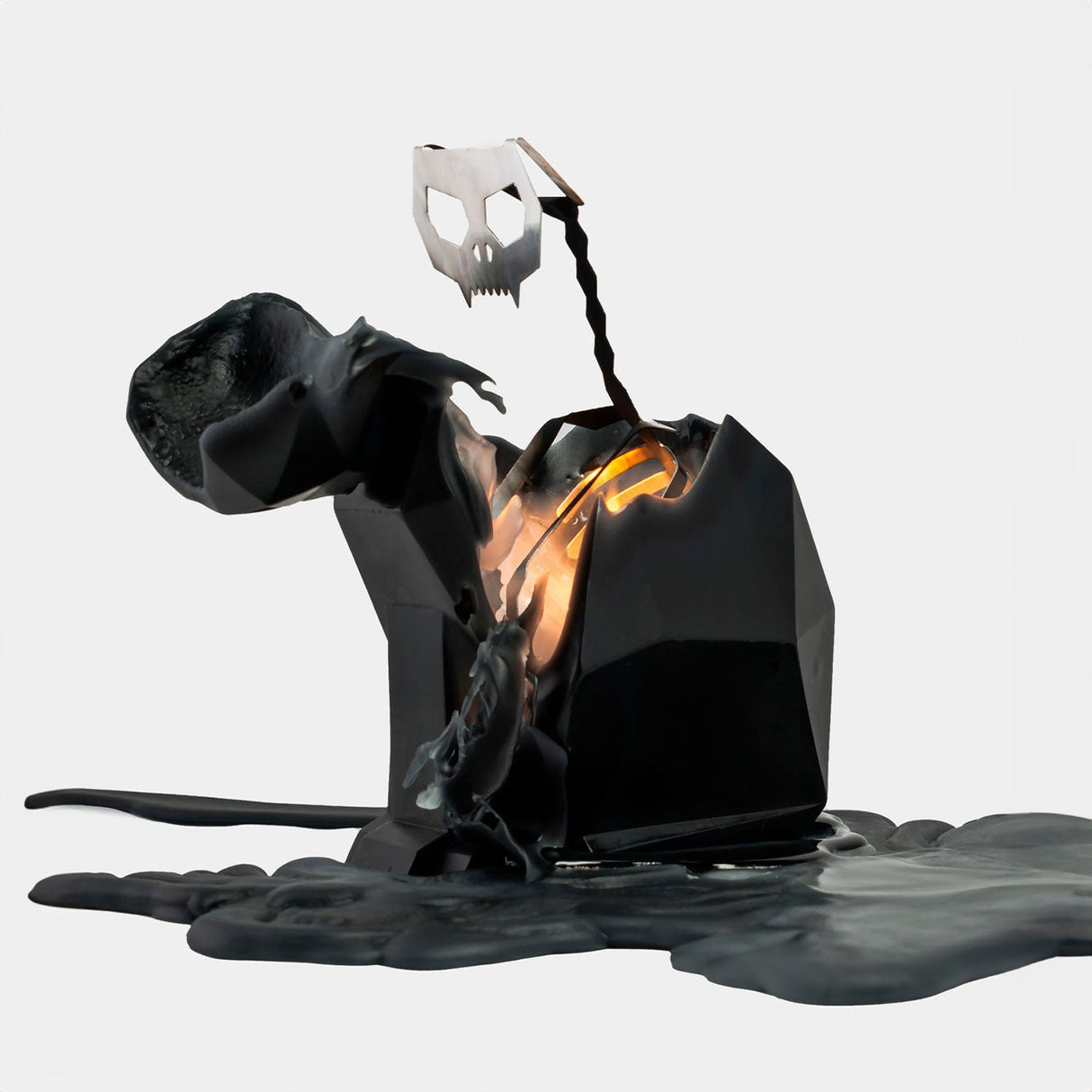 Black abstract sculpture with a metallic skull-like figure on a white background