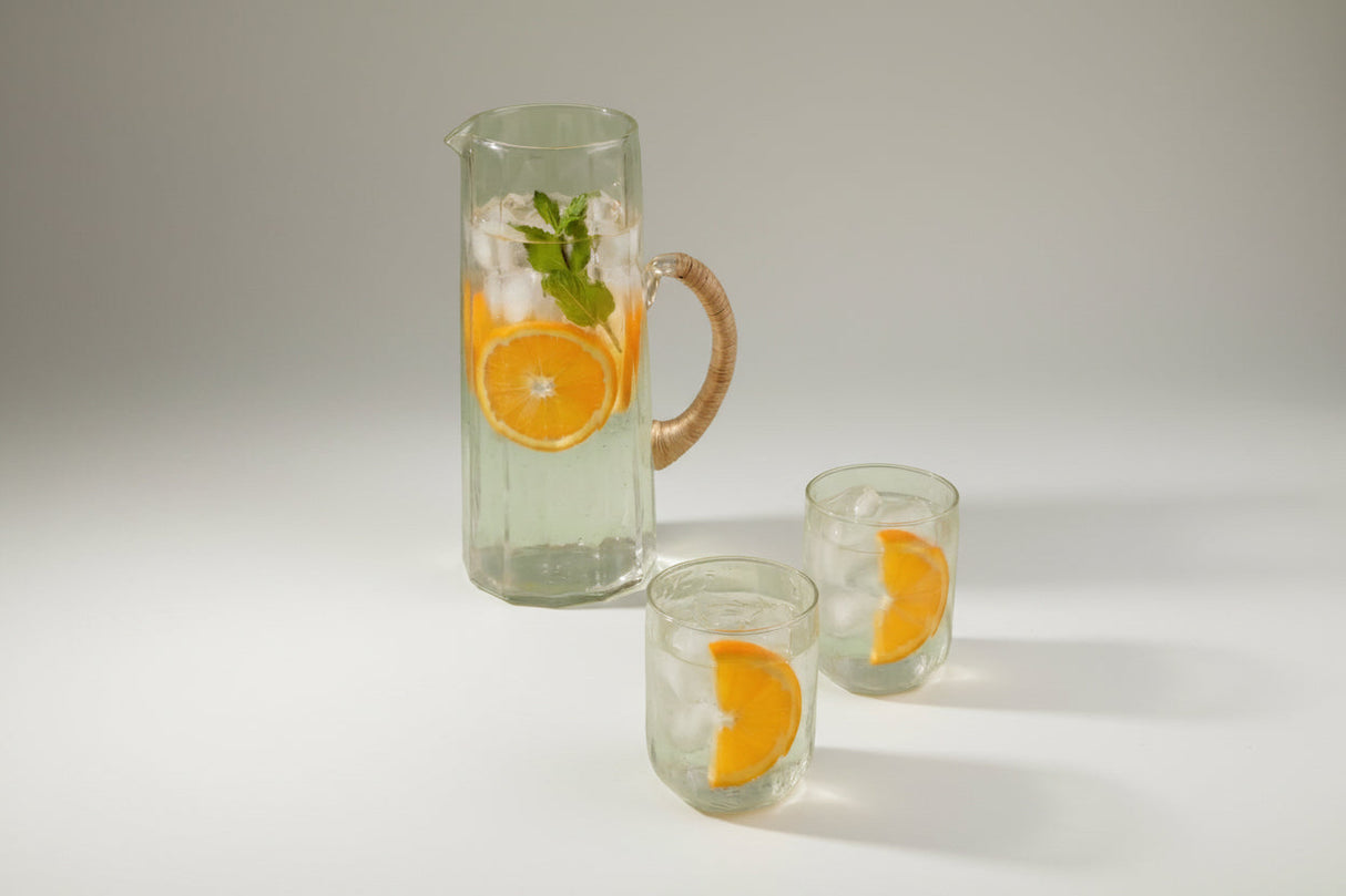 Clear pitcher and glasses with orange slices and ice on a light green background